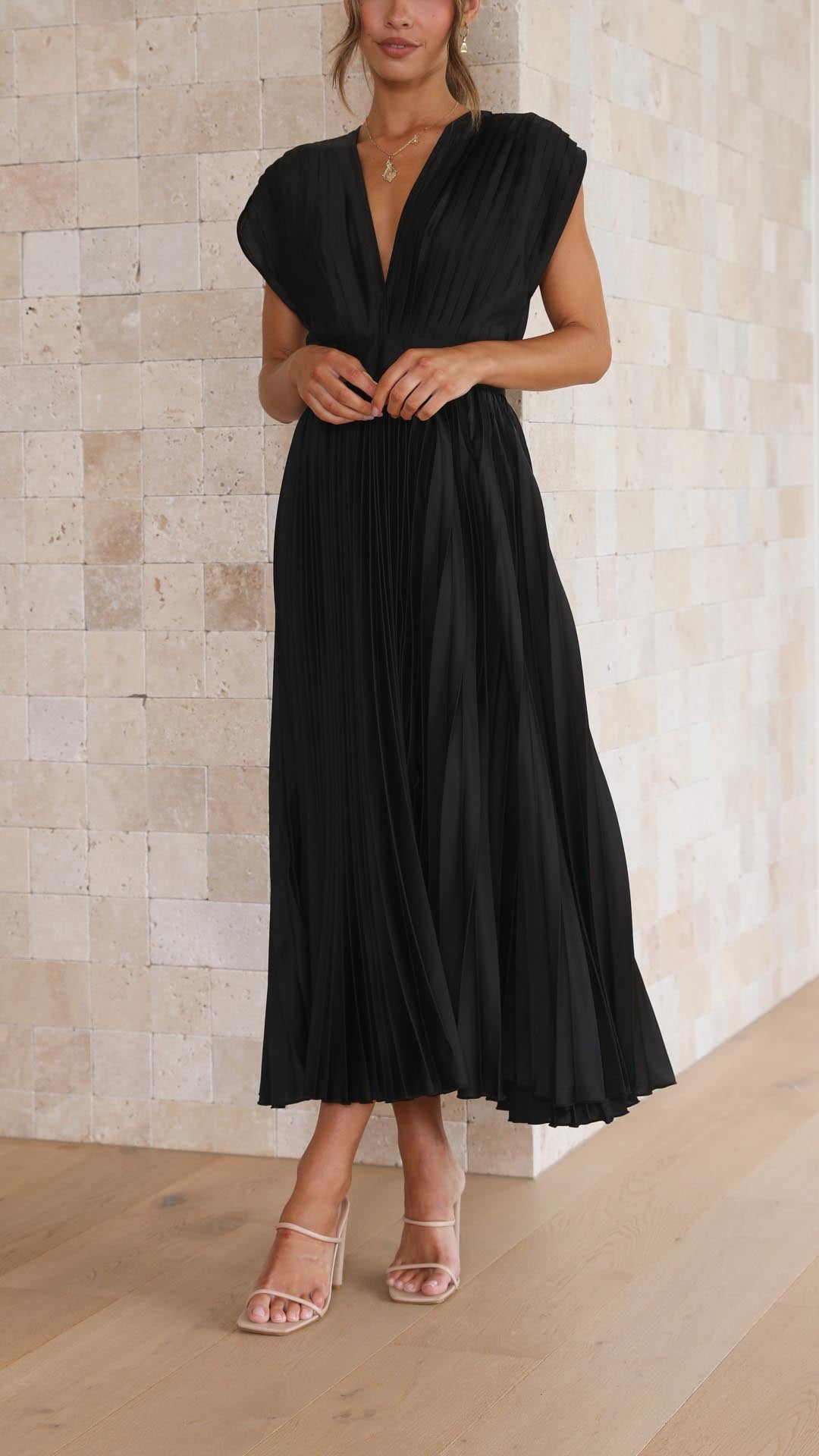 Woman wearing a black dress against a light stone wall.