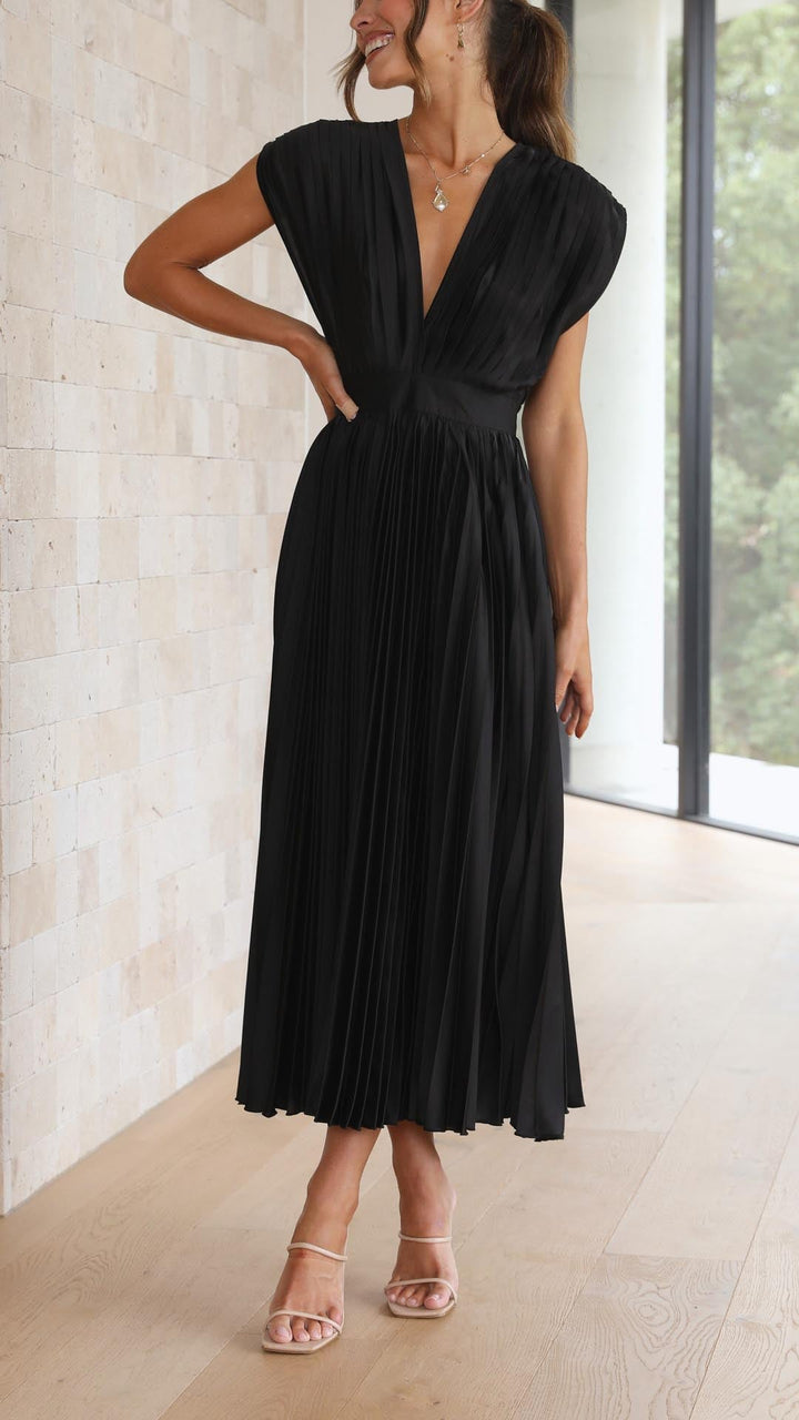 Woman wearing a black dress standing indoors with a neutral background