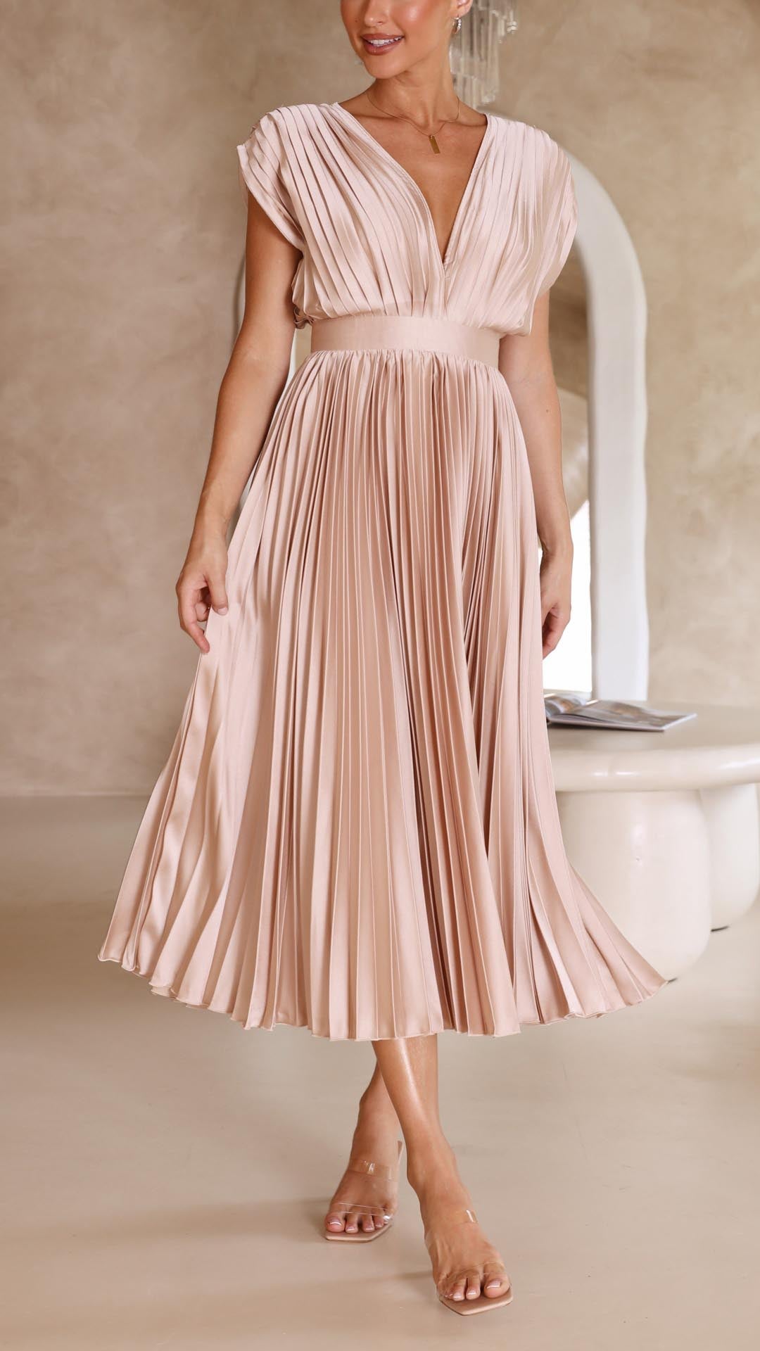 Woman wearing a blush pink pleated dress in a neutral setting