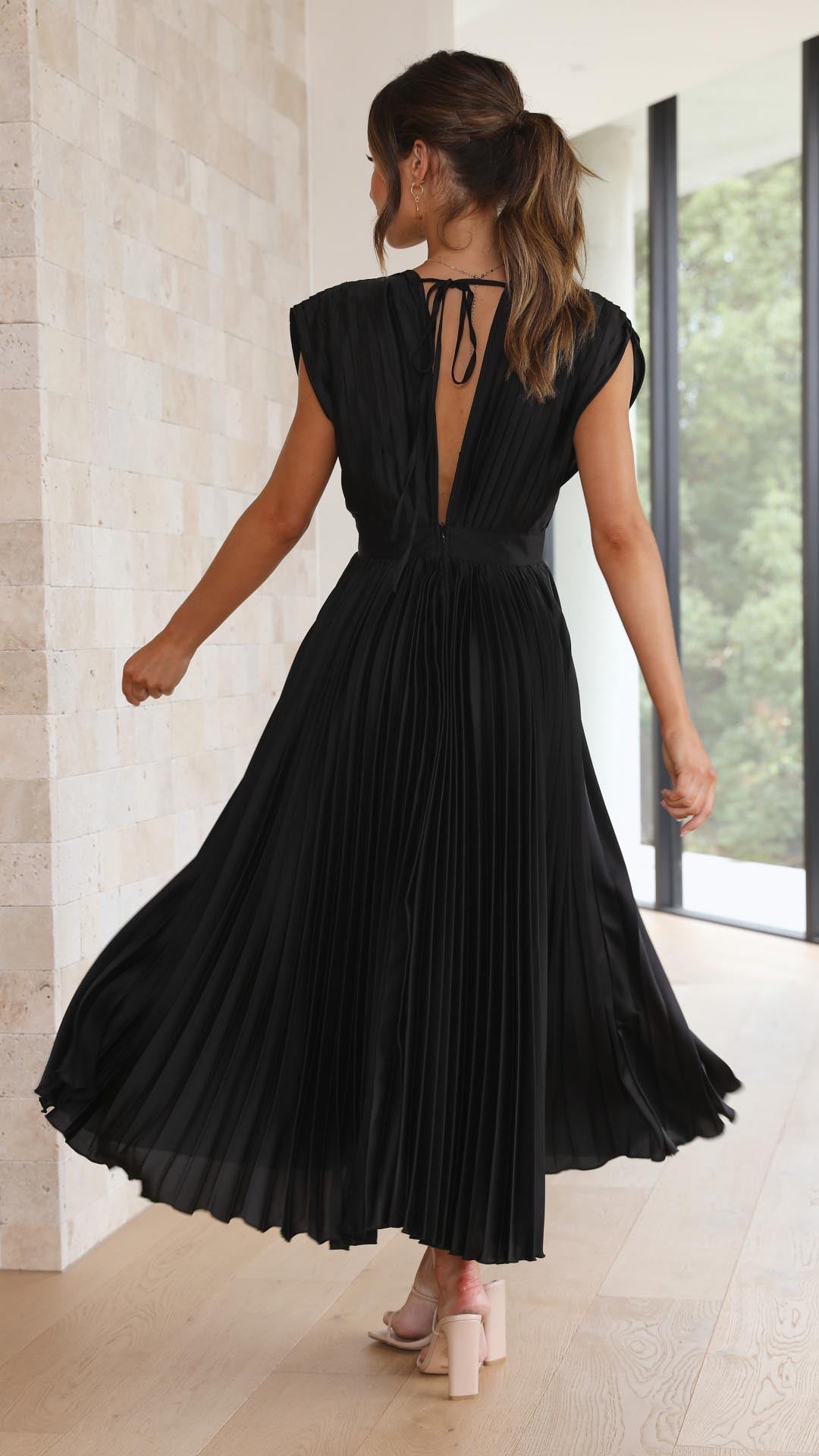 Woman wearing a black pleated dress with a flowing skirt in a modern interior setting.