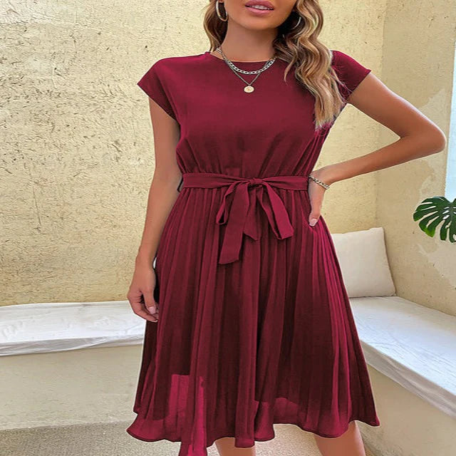 Woman wearing a burgundy dress with a belt in a room with a beige wall and white bench.