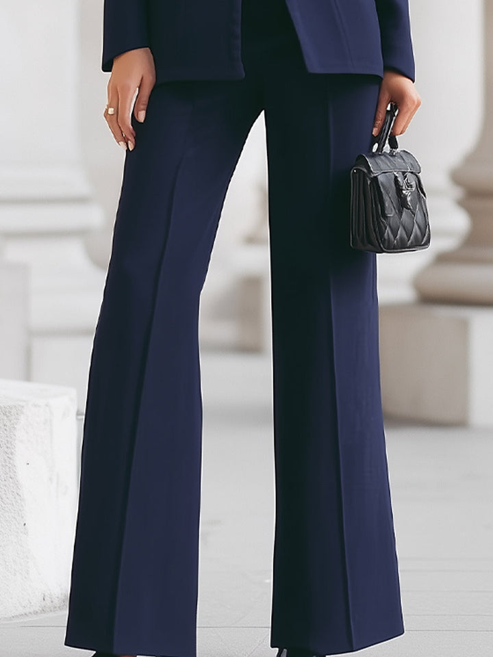 Person wearing a navy blue suit with wide-leg pants holding a black handbag.